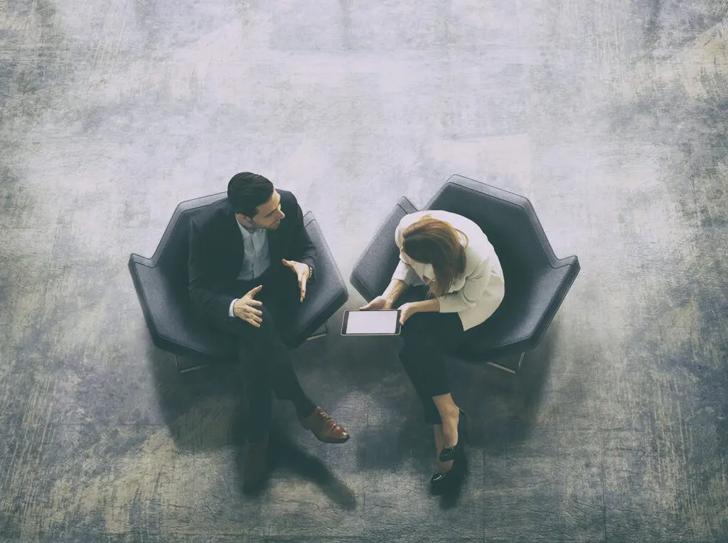 A high-angle view of a businessman and a businesswoman sitting in the office building lobby and using a digital tablet